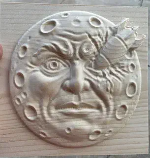 A detailed moon face bas relief carved into a square wood panel